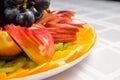 Sliced fruit - apples, oranges, kiwi topped with grapes on white dish Royalty Free Stock Photo