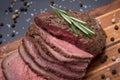 Sliced Grass Fed juicy Corn Roast Beef garnished with Fresh Rosemary Herb and Rainbow Peppercorns on wood cutting board.