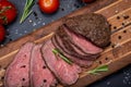 Sliced Grass Fed juicy Corn Roast Beef garnished with Tomatoes, Fresh Rosemary Herb and Rainbow Peppercorns on natural wooden cutt
