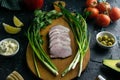 Sliced ham on a wooden board, around the ham, green onions, tomato, souce, olives, lemon, spice, dill and parsley Royalty Free Stock Photo