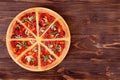 Sliced hot pizza with salami, arugula, tomatoes, mushrooms and texas spice mix, on a round wood platter which is on wood Royalty Free Stock Photo