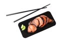 Sliced marinated salmon fillet wrapped in nori seaweed sheets with wasabi on black paper and wooden chopsticks