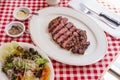 Sliced medium rare charcoal grilled wagyu Ribeye steak in white plate on red and white pattern tablecloth with salad and cutlery