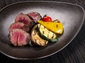 Sliced medium rare filet mignon served with grilled vegetables on a plate on dark background Royalty Free Stock Photo