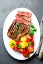 Sliced medium rare grilled beef steak served on white plate with tomato salad and potatoes balls. Barbecue, bbq meat Royalty Free Stock Photo