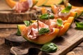 Sliced melon with ham and basil leaves, served on a wood chopping board Royalty Free Stock Photo