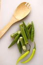 Sliced okra, green chili and a wooden spoon on a white chopping board