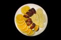 Sliced orange, apple and lemon slices on a white fruit plate on a black background Royalty Free Stock Photo