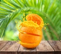 Sliced orange fruit splashing about orange juice on the wooden table. Green palm leaves at the background Royalty Free Stock Photo