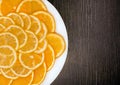 Sliced orange and lemon in a white plate on a dark wooden texture background, copy space Royalty Free Stock Photo