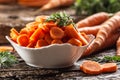 Sliced pieces of carrot in a bowl and a fresh bunch of carrots in the background