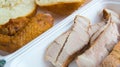 Sliced pieces of cold baked pork in a plastic container, with slices of wheat bread and fried chicken wing, an Royalty Free Stock Photo