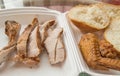 Sliced pieces of cold baked pork in a plastic container, with slices of wheat bread and fried chicken wing, an Royalty Free Stock Photo
