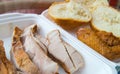 Sliced pieces of cold baked pork in a plastic container, with slices of wheat bread and fried chicken wing, an Royalty Free Stock Photo