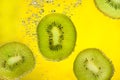 Sliced pieces of kiwi covered with bubbles falling in water on yellow background Royalty Free Stock Photo