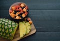 Sliced pineapple and bowl of fruits on black wooden background. Copy space Royalty Free Stock Photo