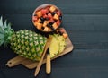 Sliced pineapple and bowl of fruits on black wooden background Royalty Free Stock Photo