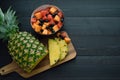 Sliced pineapple and bowl of fruits on black wooden background. Top view Royalty Free Stock Photo