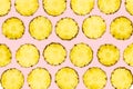 Sliced pineapple pieces lay in pattern on isolated light pink ba