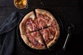 Sliced pizza with prosciutto and mozzarella cheese and a glass of white wine with a napkin on a black table. View from above. Royalty Free Stock Photo