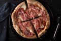 Sliced pizza with prosciutto and mozzarella cheese with a napkin on a black table. View from above. Royalty Free Stock Photo