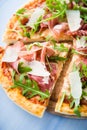 Sliced pizza with prosciutto parma ham, arugula (salad rocket) and parmesan on blue wooden background close up Royalty Free Stock Photo