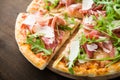 Sliced pizza with prosciutto parma ham, arugula (salad rocket) and parmesan on dark wooden background close up Royalty Free Stock Photo