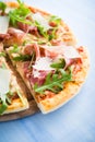 Sliced pizza with prosciutto (parma ham), arugula (salad rocket) and parmesan on blue wooden background Royalty Free Stock Photo