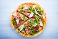 Sliced pizza with prosciutto (parma ham), arugula (salad rocket) and parmesan on blue wooden background Royalty Free Stock Photo