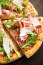 Sliced pizza with prosciutto (parma ham), arugula (salad rocket) and parmesan on dark wooden background Royalty Free Stock Photo