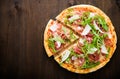 Sliced pizza with prosciutto (parma ham), arugula (salad rocket) and parmesan on dark wooden background Royalty Free Stock Photo