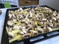 Sliced potatoes and mushrooms for roasting in the oven are laid on the baking tray.