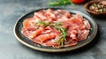Thinly sliced prosciutto garnished with fresh rosemary on a dark plate