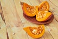 Sliced pumpkin with fresh seeds on the brown plate on the wooden background. Ingredients for tasty diet autumn dish