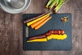 Sliced rainbow carrots on a black cutting board, stainless-steel bowl, wood table Royalty Free Stock Photo