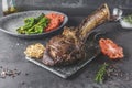 Sliced rare grilled or barbecued tomahawk beef steak on a griddle with fresh rosemary and tomato in a close up view. Royalty Free Stock Photo