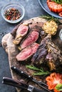 Sliced rare grilled or barbecued tomahawk beef steak on a griddle with fresh rosemary and tomato in a close up view. Royalty Free Stock Photo