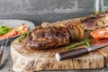 Sliced rare grilled or barbecued tomahawk beef steak on a griddle with fresh rosemary and tomato in a close up view. Royalty Free Stock Photo