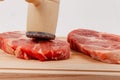 Sliced raw pork steaks meat on a cutting kitchen board on a white wooden table. above them a hammer for beating meat Royalty Free Stock Photo