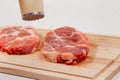 sliced raw pork steaks meat on a cutting kitchen board on a white wooden table. above them a hammer for beating meat Royalty Free Stock Photo