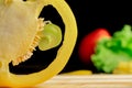 Sliced rings of fresh raw yellow bell peppers, green lettuce and red tomato on wooden board. Sweet pepper slices with Royalty Free Stock Photo