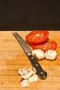 Sliced ripe, local tomatoes and mushrooms on a wood cutting board with a knife with a serrated blade Royalty Free Stock Photo