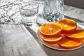 Sliced ripe oranges on plate, water glass and bottle on neutral beige table background with aesthetic sunlight shadows, healthy Royalty Free Stock Photo