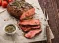 Sliced Roast beef on white paper on wooden table with grilled vegetables. Royalty Free Stock Photo