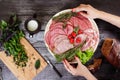 Sliced sausage, hands holding the dish, wooden countertop, chopped basil Royalty Free Stock Photo