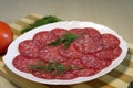 Sliced sausage on a white plate with dill on a wooden board.