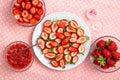 Sliced strawberries on a white plate, strawberry jam and other sweet berries on a pink tablecloth