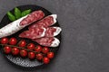 Sliced thin catalan fuet sausage and bunch of red cherry tomatoes on a black plate over dark rough surface. Traditional spanish Royalty Free Stock Photo
