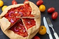 Sliced tomato galette or tart with onion rings on the dark wooden board decorated with various cherry tomatoes