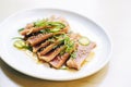 sliced tuna steak with green onions and sesame oil on white plate